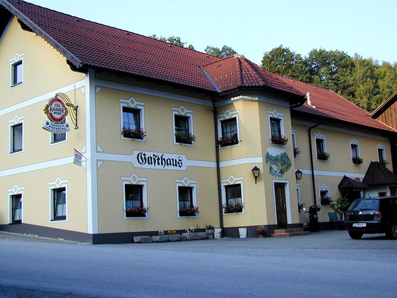 Tradiční hostinec se žlutou fasádou a červenými střešními taškami.