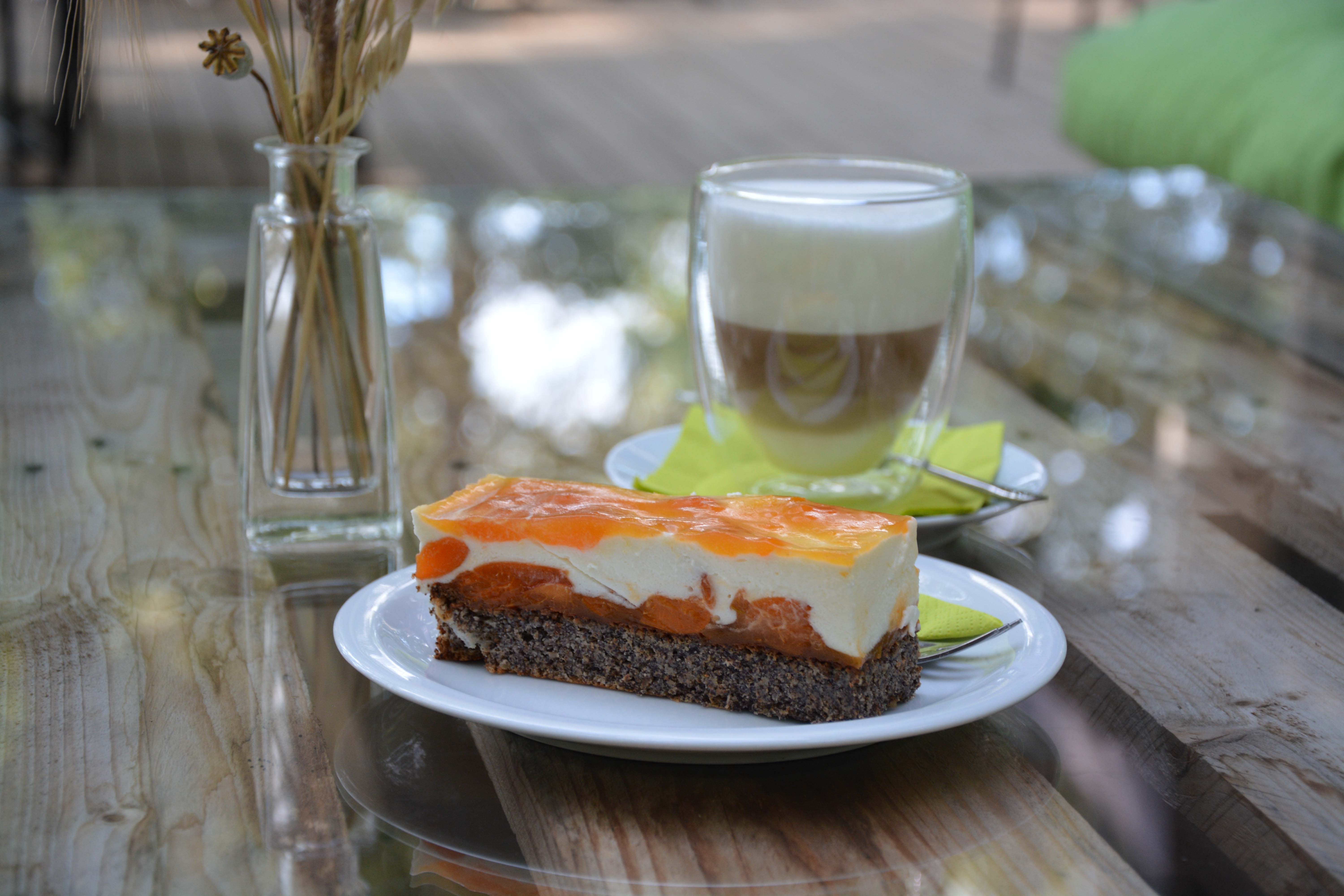 Talíř s ovocným dortem na dřevěném stole, v pozadí sklenice s kávou a váza.