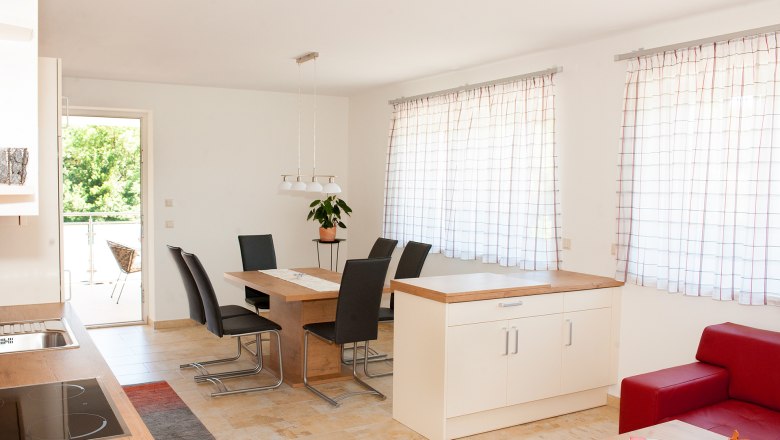 Modern&iacute; j&iacute;deln&iacute; kout s dřevěn&yacute;m stolem, čern&yacute;mi židlemi a velk&yacute;mi okny se z&aacute;věsy.