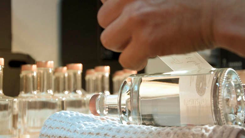 Detailní záběr na ruku, která lepí etiketu na láhev brandy.