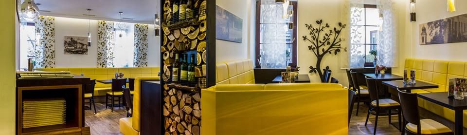 Pohled do interiéru restaurace se žlutými lavicemi a dekorativními prvky.