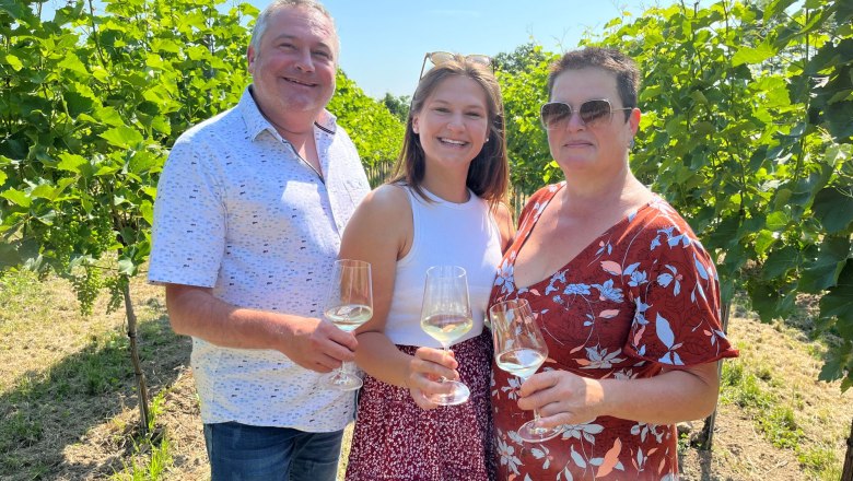 Rodina Heimelov&yacute;ch se skleničkami na v&iacute;no v ruce. Rodina stoj&iacute; mezi vinnou r&eacute;vou.