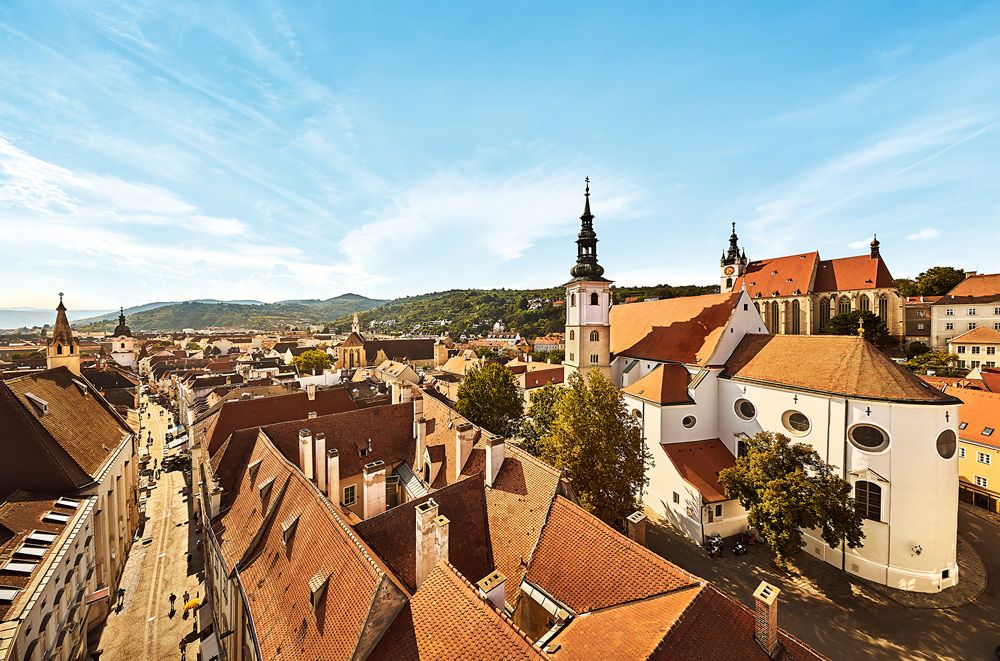 Panoramatický pohled na staré centrum Kremže s kostely a červenými střechami.