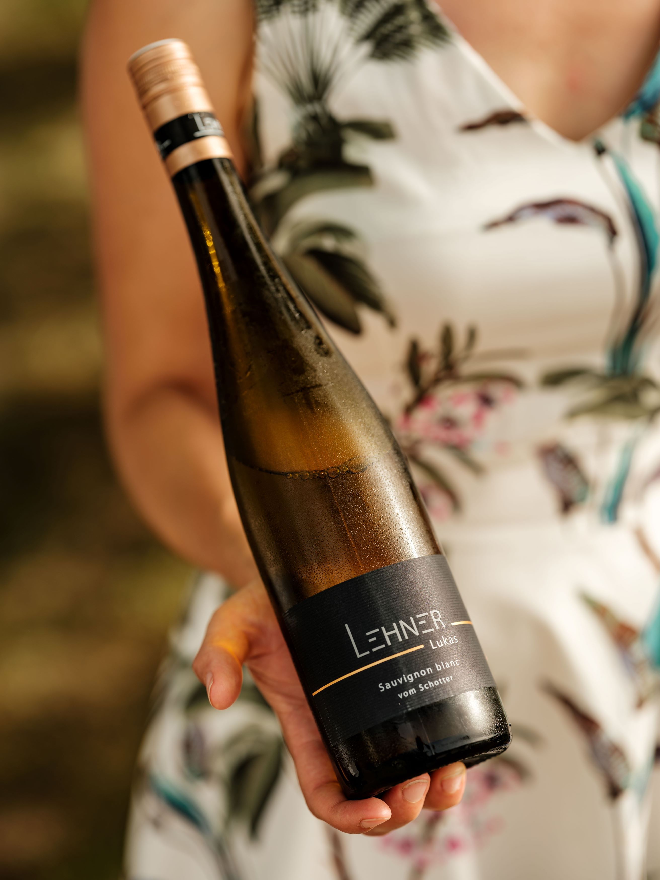 Jedna osoba drží láhev vína s etiketou "Lehner Lukas Sauvignon blanc vom Schotter".