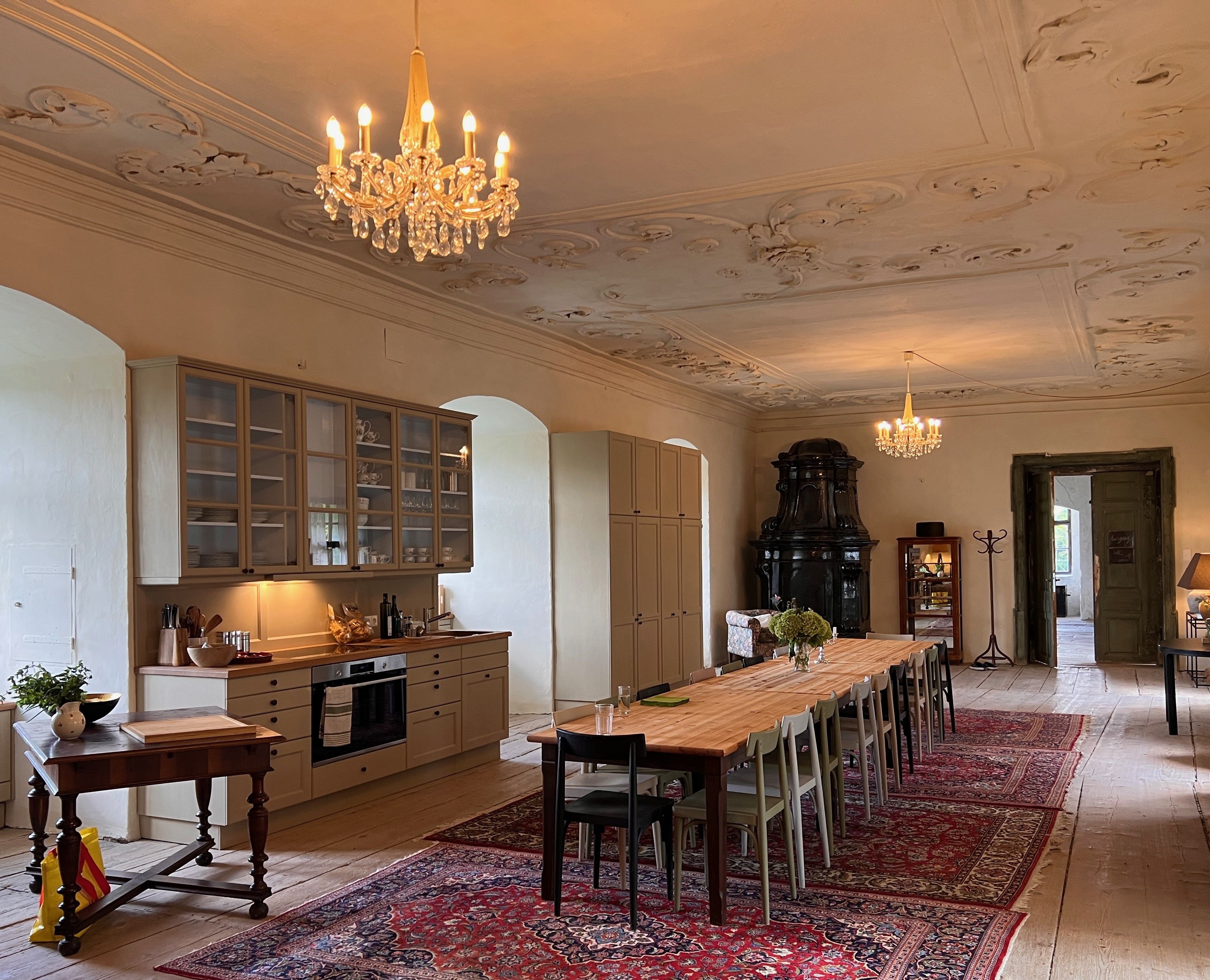 Elegantní jídelna s dlouhým dřevěným stolem, lustry a starožitnými kamny.