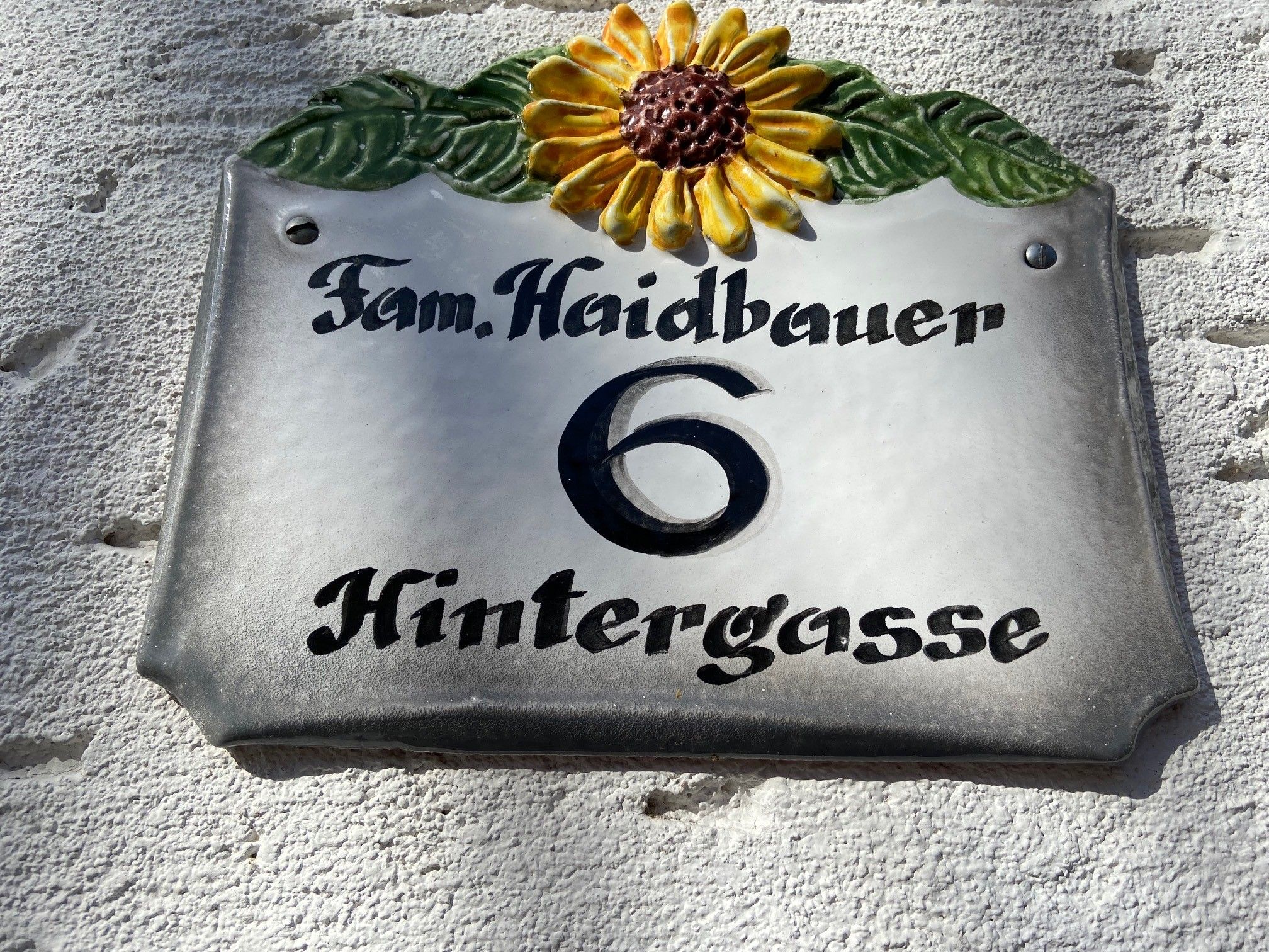 Domovní znamení se slunečnicí a nápisem "Fam. Haidbauer 6 Hintergasse".
