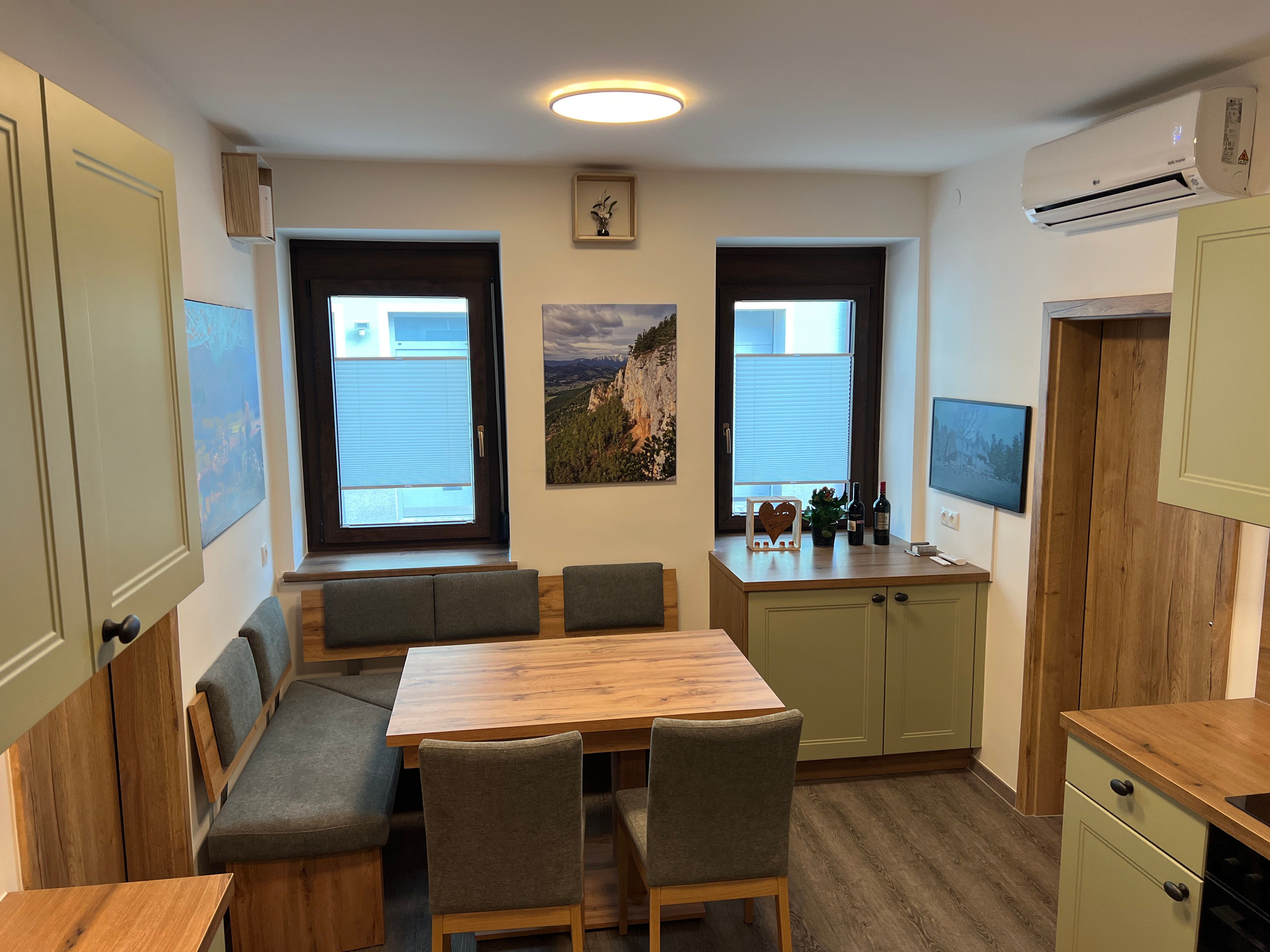 Moderní kuchyně s dřevěným nábytkem, jídelním stolem a zelenými skříňkami.