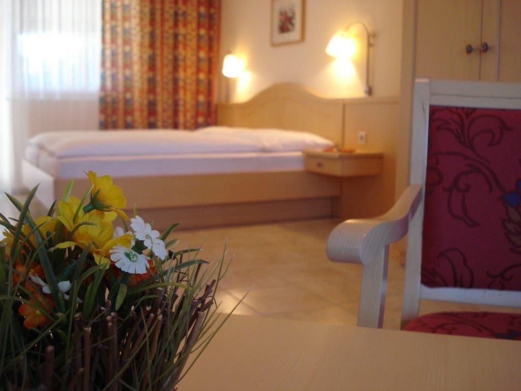 Útulný pokoj pro hosty s postelí, židlí a stolem s květinami.