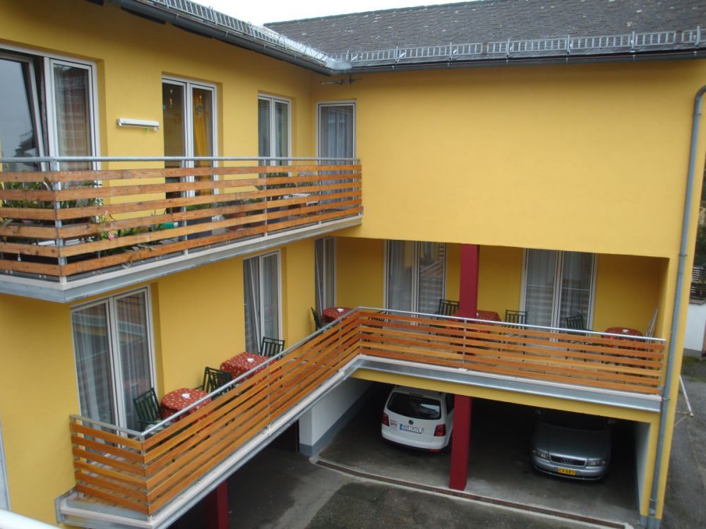 Žlutá budova s balkony a zaparkovanými auty pod nimi.
