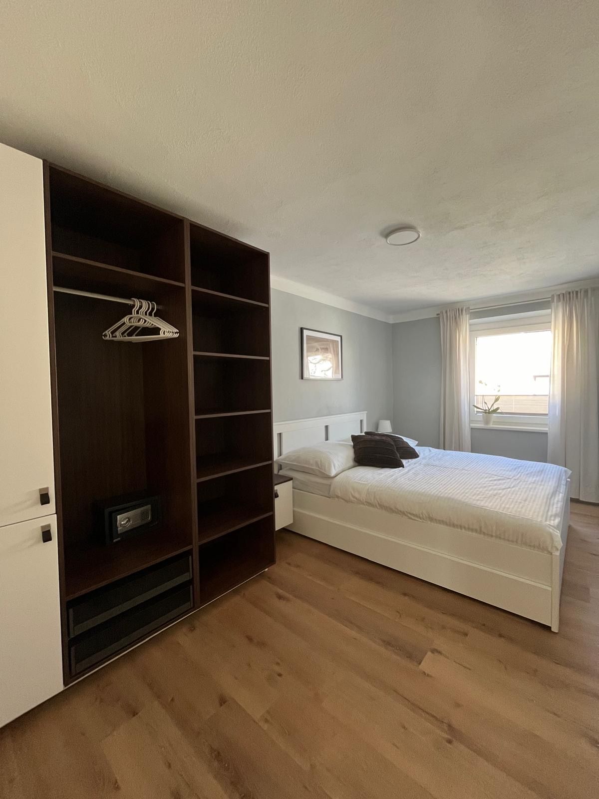 Moderní ložnice s manželskou postelí, šatní skříní a oknem se závěsy.