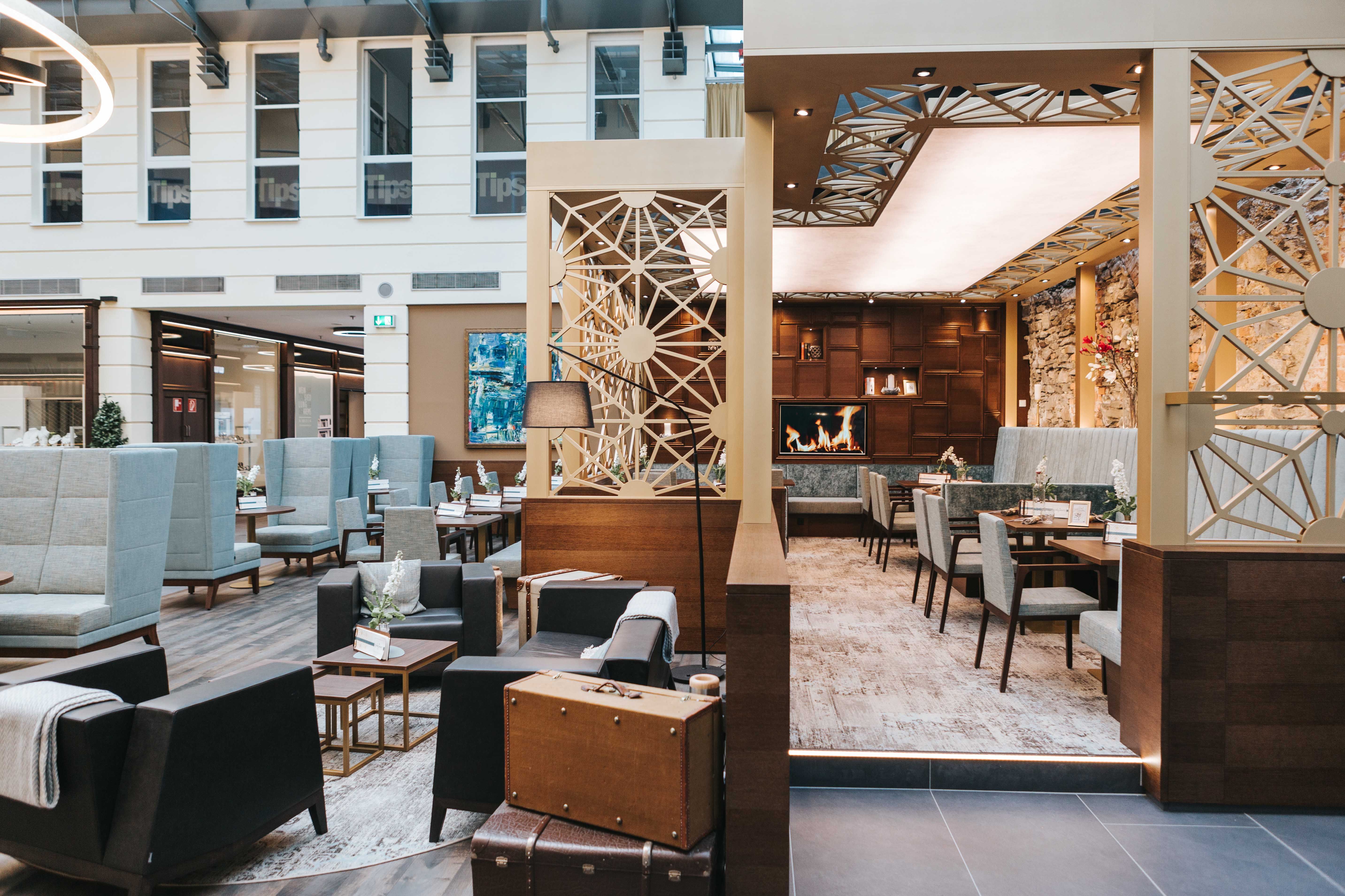 Pohled do interiéru moderní kavárny s útulným posezením, krbem a stylovou výzdobou.