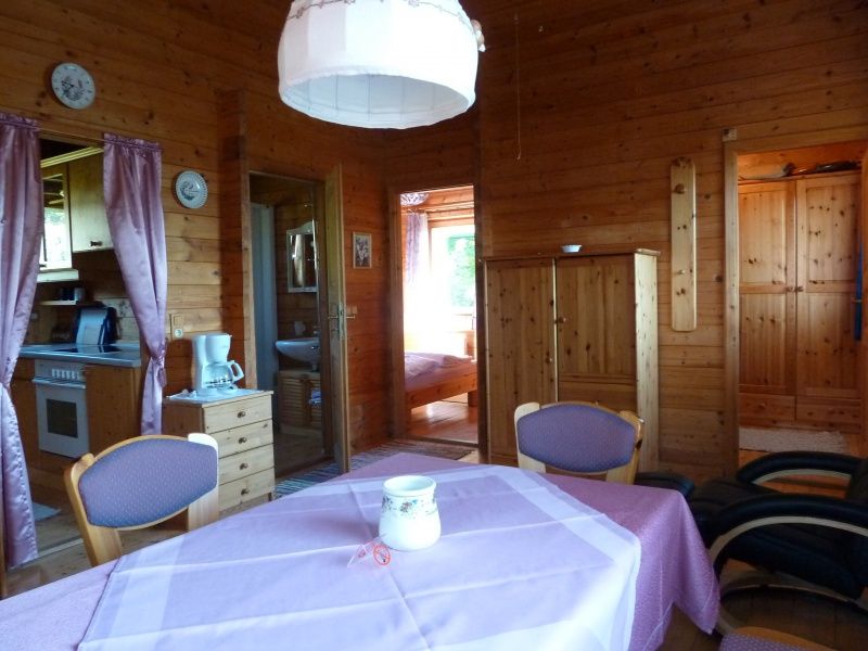 Pohled do interiéru útulného rekreačního domu s dřevěnými stěnami, jídelním stolem a kuchyňským koutem.