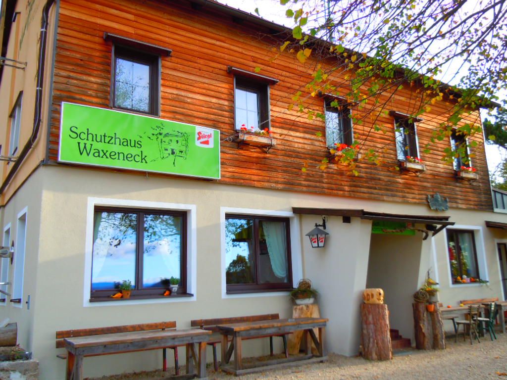 Vchod do přístřešku Waxeneck s dřevěnými stoly a květinovými truhlíky.
