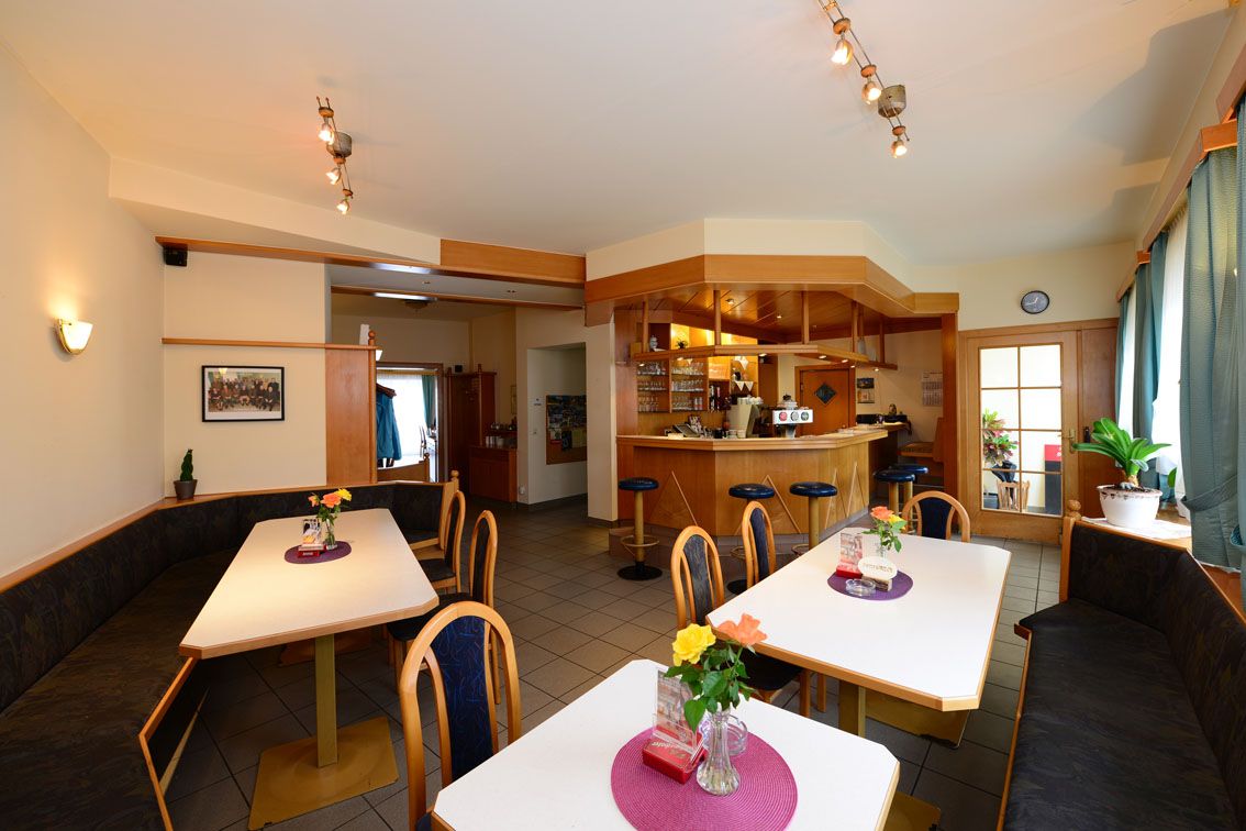 Pohled do interiéru útulné restaurace se stoly, židlemi a barem.