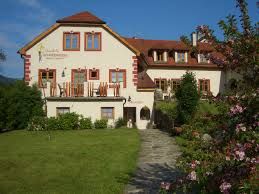 Velký tradiční dům s červenou střechou a kvetoucí zahradou v popředí.