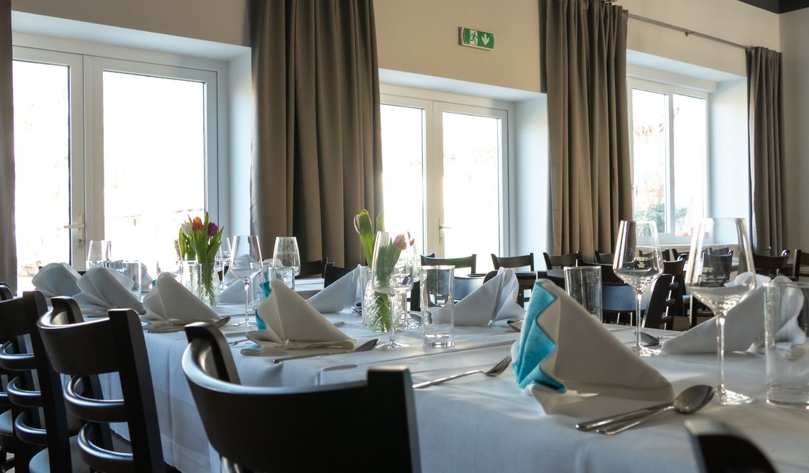 Elegantní restaurace s prostřenými stoly, bílými ubrusy a skládanými ubrousky.