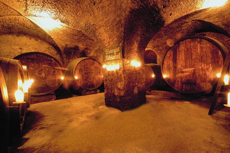 Historický vinný sklep s velkými dřevěnými sudy a světlem svíček.