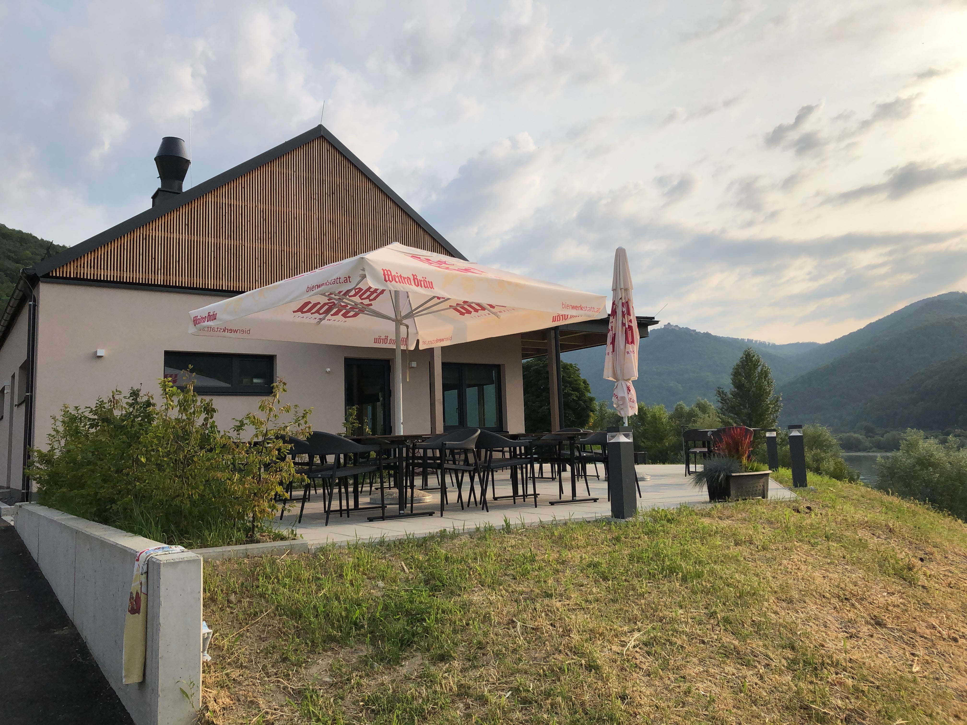 Moderní terasa se slunečníkem, obklopená zelenou krajinou a kopci.