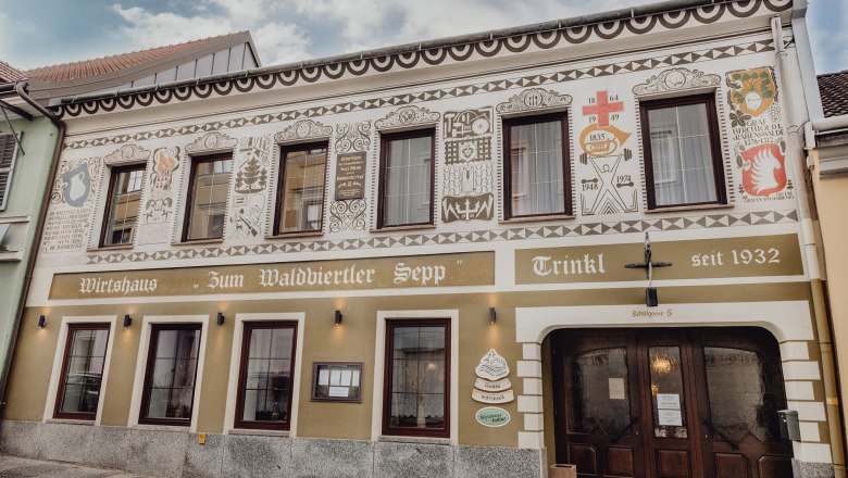 Fasáda tradičního hostince s dekorativními malbami a nápisem "Zum Waldviertler Sepp" ve Schremsu.