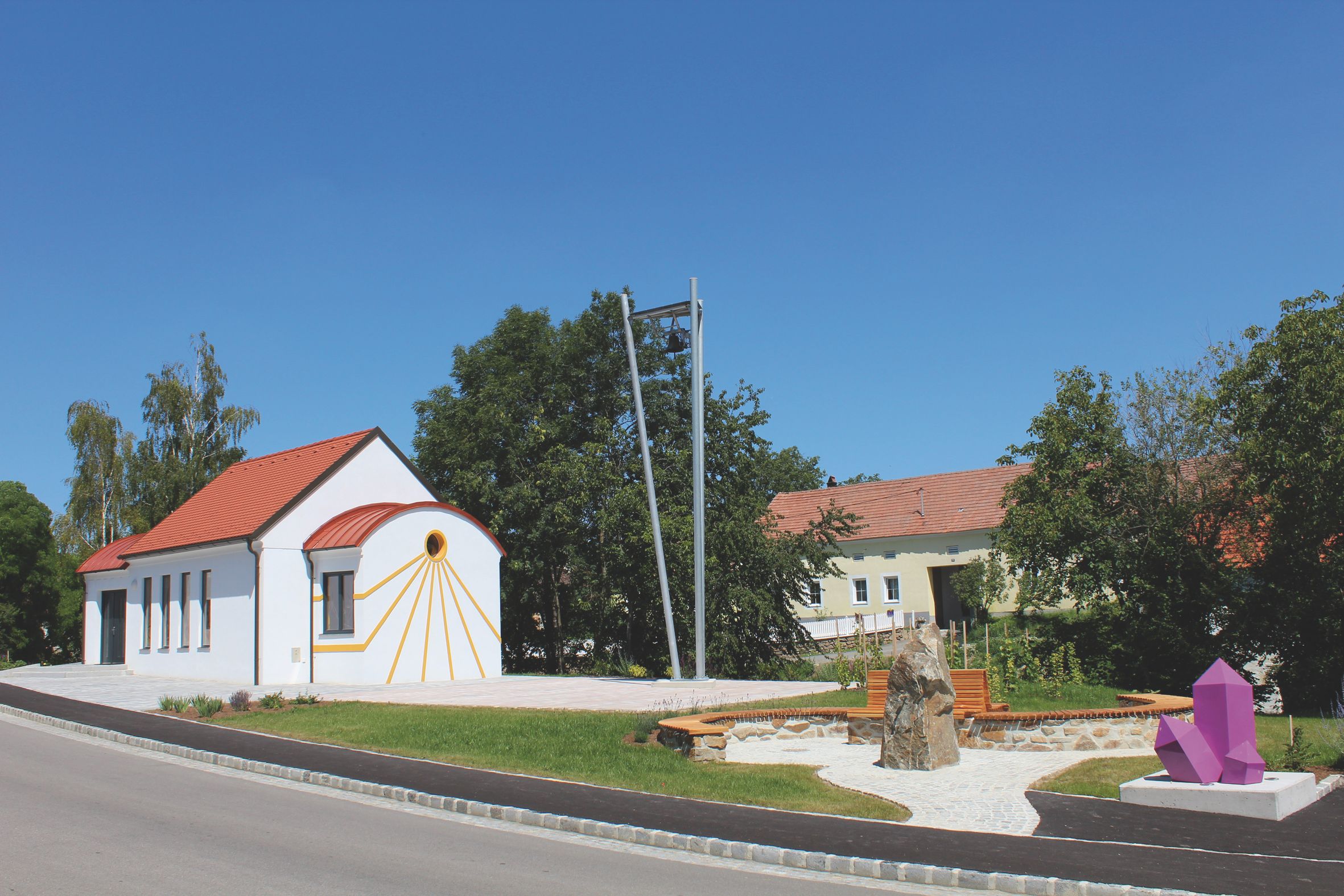 Bílá kaple s červenou střechou a ametystovou sochou v popředí.