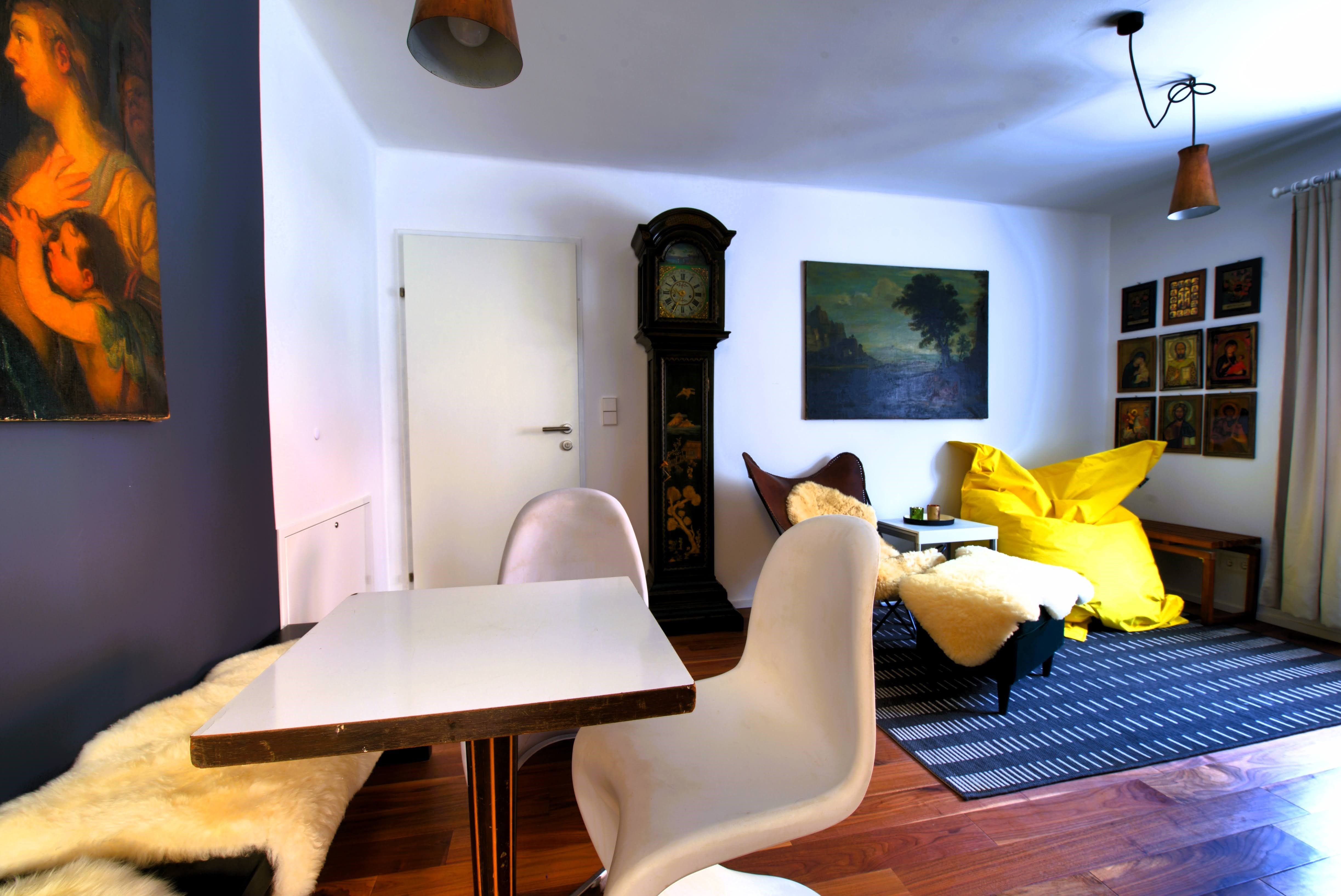 Obývací pokoj se stolem, židlemi, dědečkovými hodinami, obrazy a žlutým beanbagem.