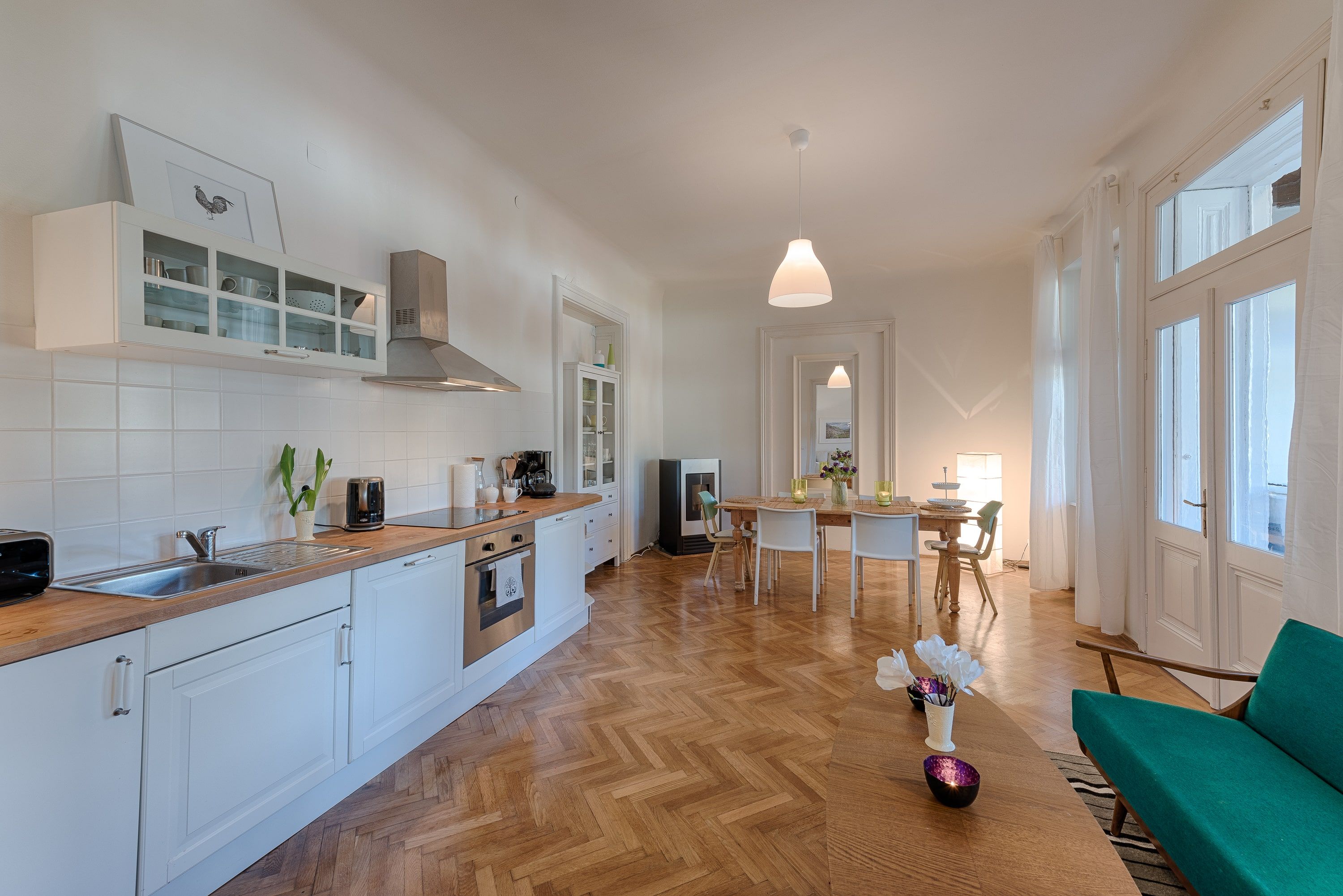 Moderní kuchyně s jídelním stolem, bílými skříňkami a dřevěnou podlahou.