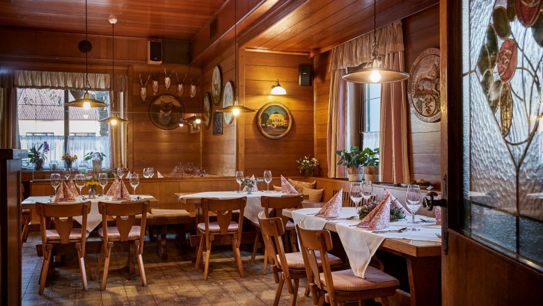 Útulná, dřevem obložená hospoda s prostřenými stoly, židlemi a dekorativními prvky na stěnách.