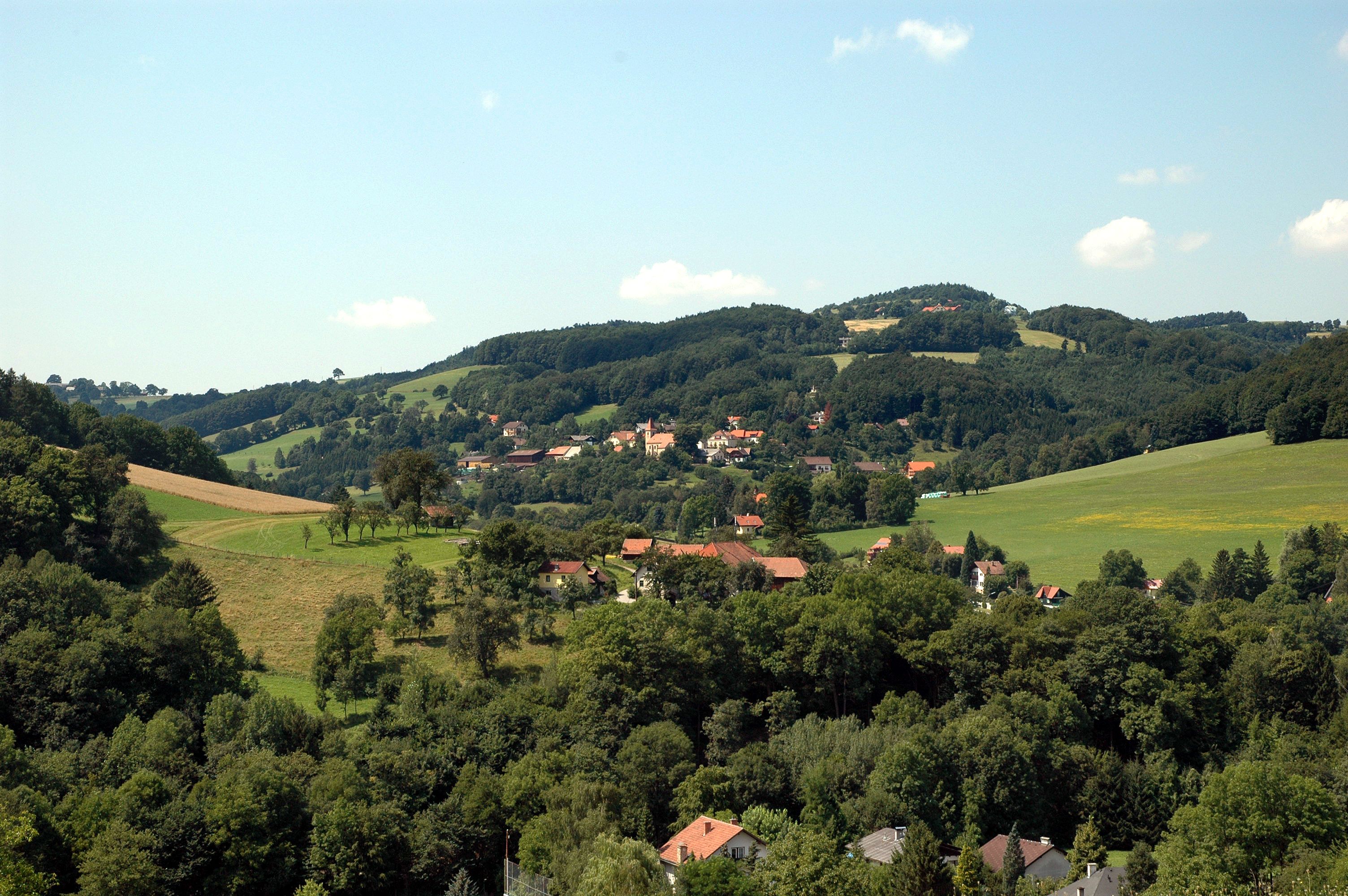 Krajina s kopci, lesy a vesnicí v pozadí.