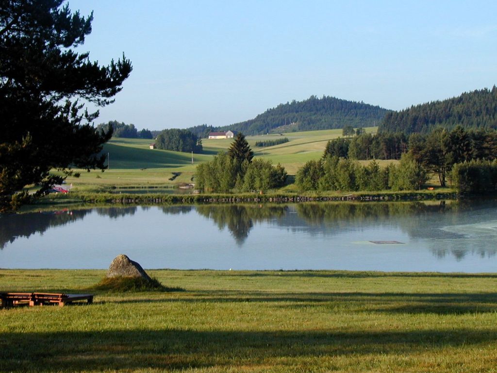 Klidné jezero s okolními loukami a lesy ve venkovské krajině.