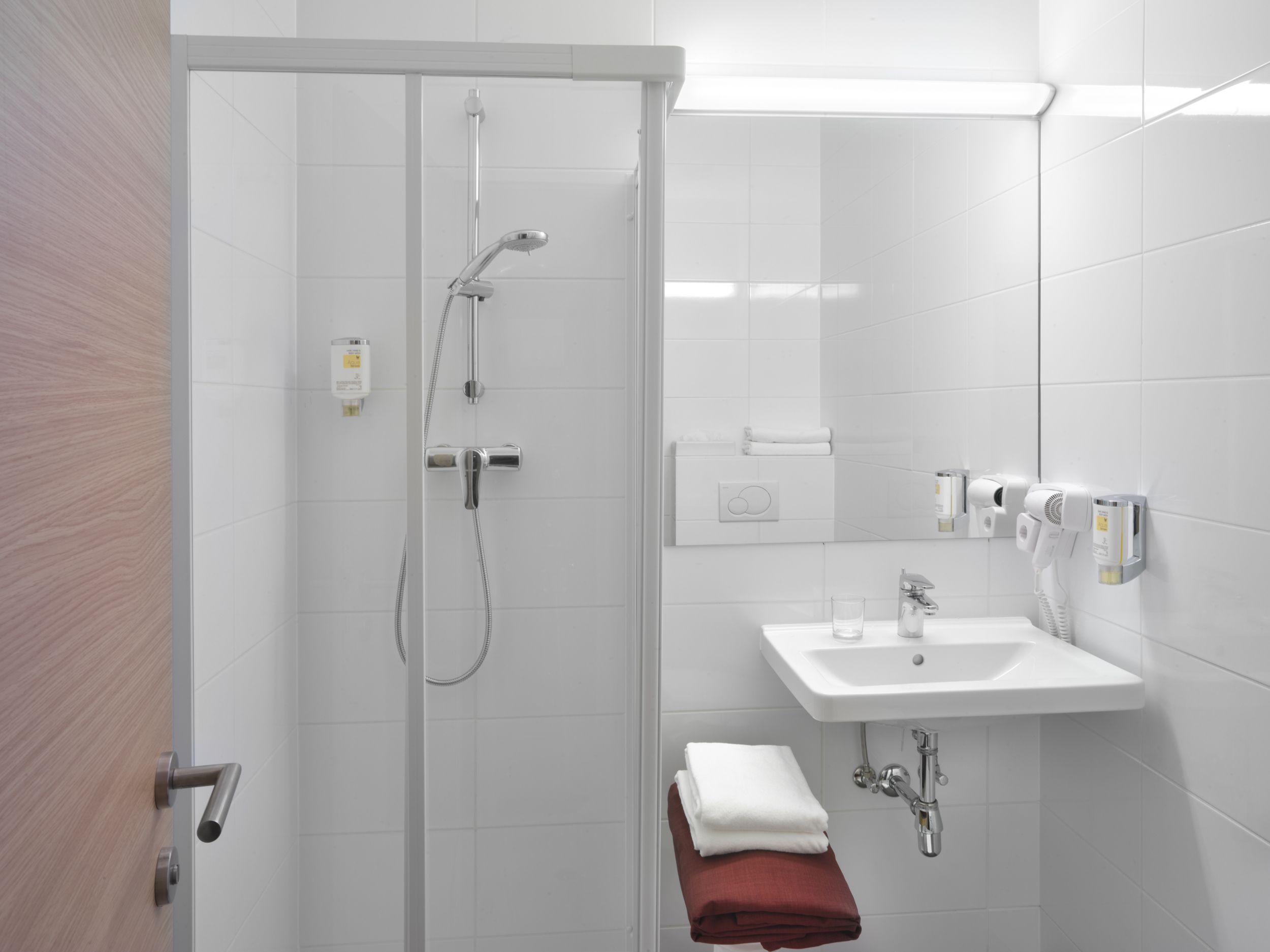 Moderní hotelová koupelna se sprchou, umyvadlem a ručníky.