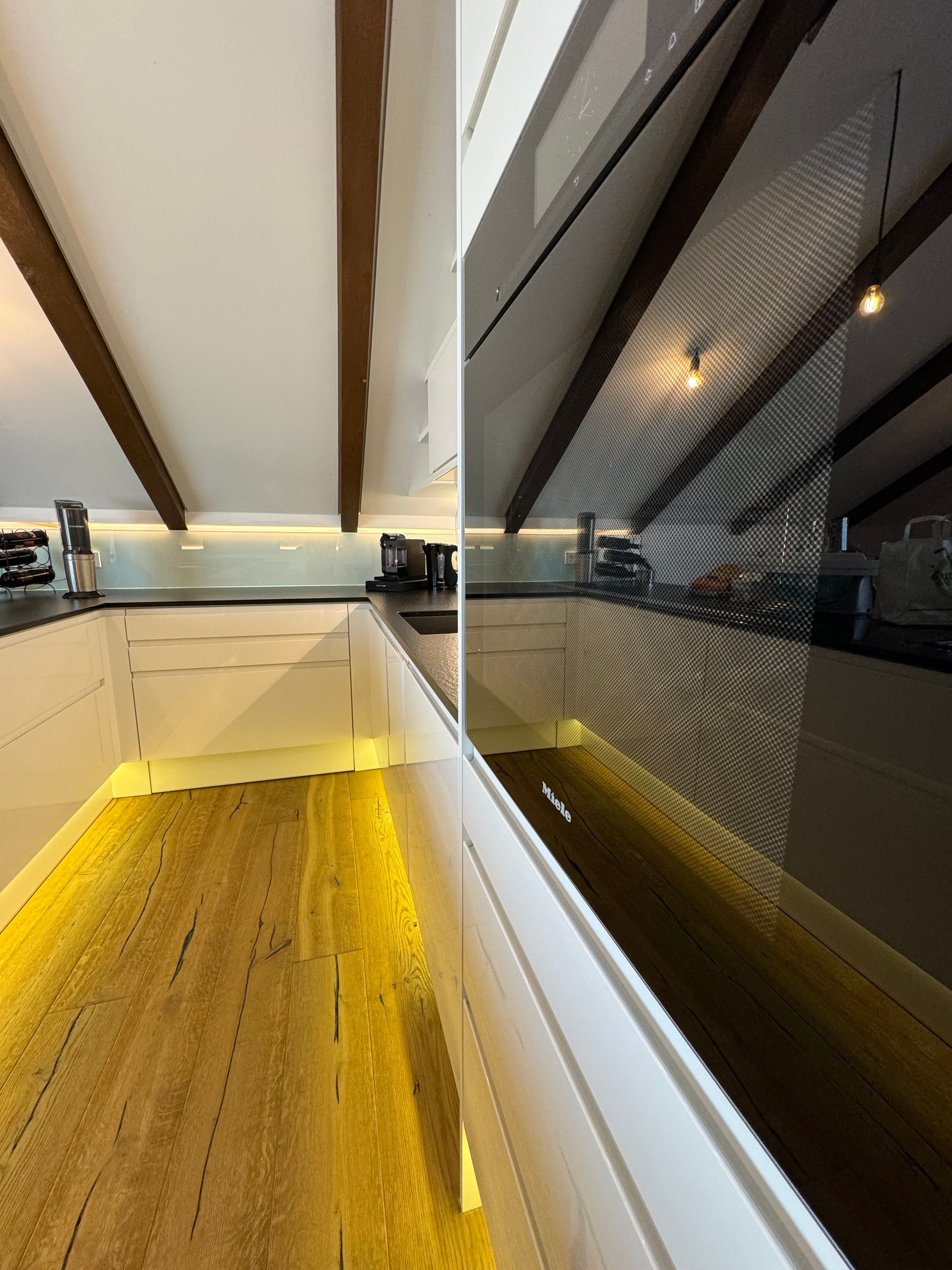 Moderní kuchyně s dřevěnou podlahou, bílými skříňkami a vestavěnou troubou.