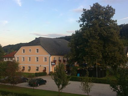 Pohled na žlutý hostinec s velkým stromem a parkovištěm.