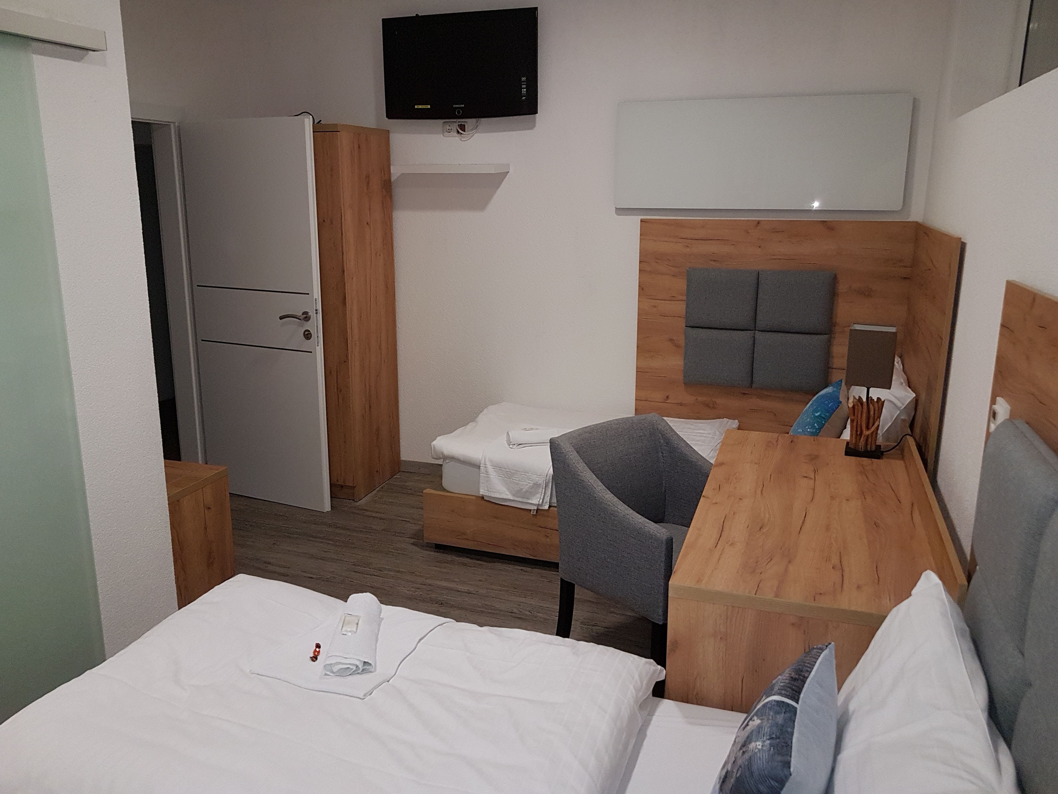 Hotelový pokoj s dřevěným nábytkem, dvěma postelemi, psacím stolem a televizí na stěně.