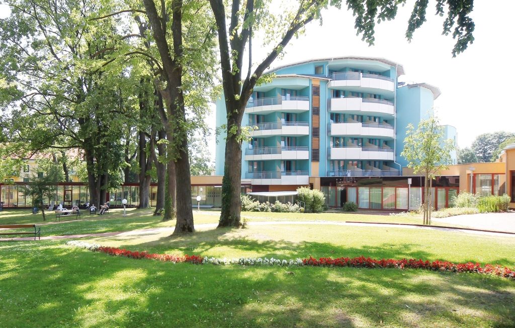 Moderní budova s balkony a zahradou v popředí.