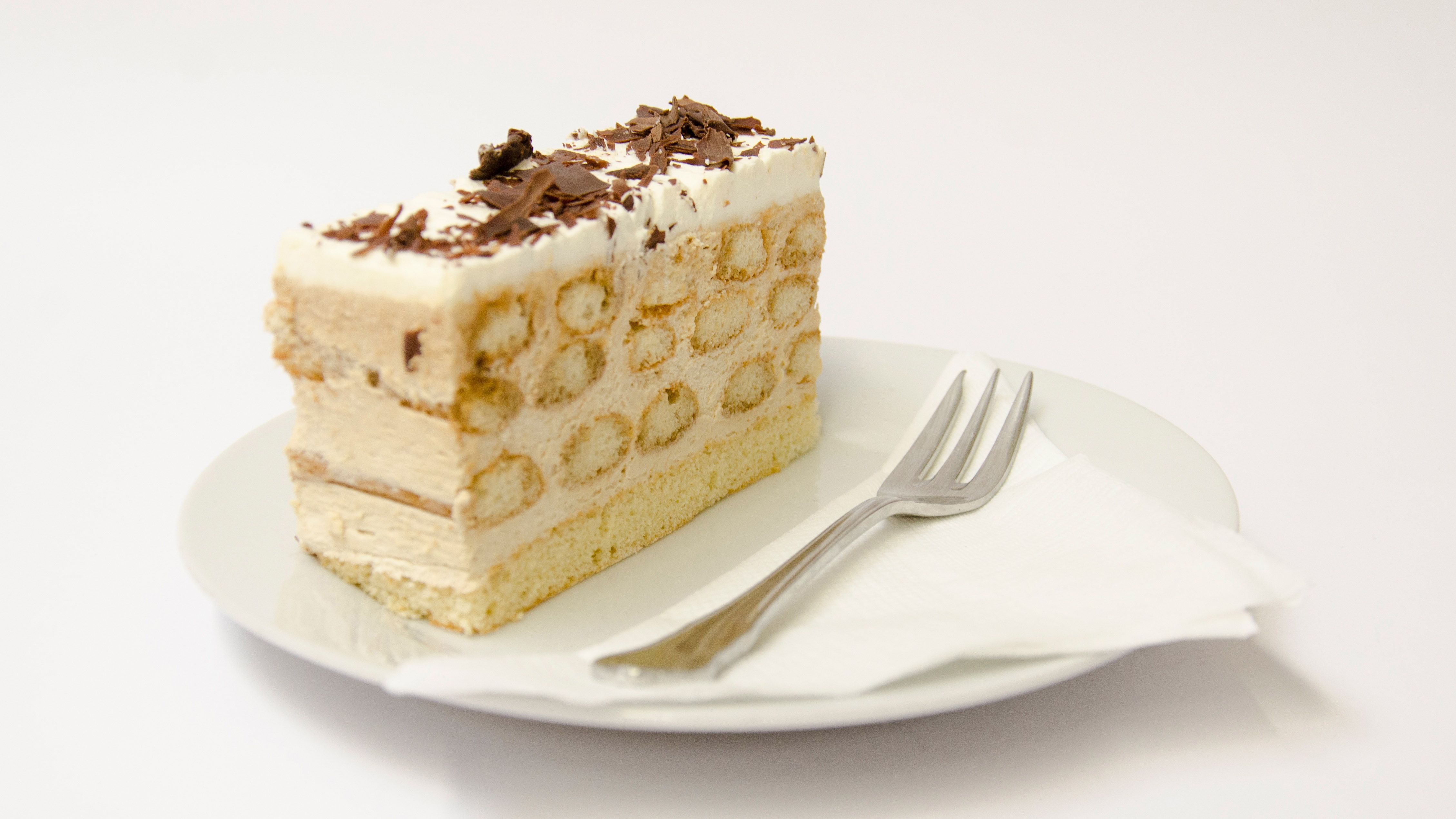 Kousek dortu Malakoff na talíři s vidličkou.