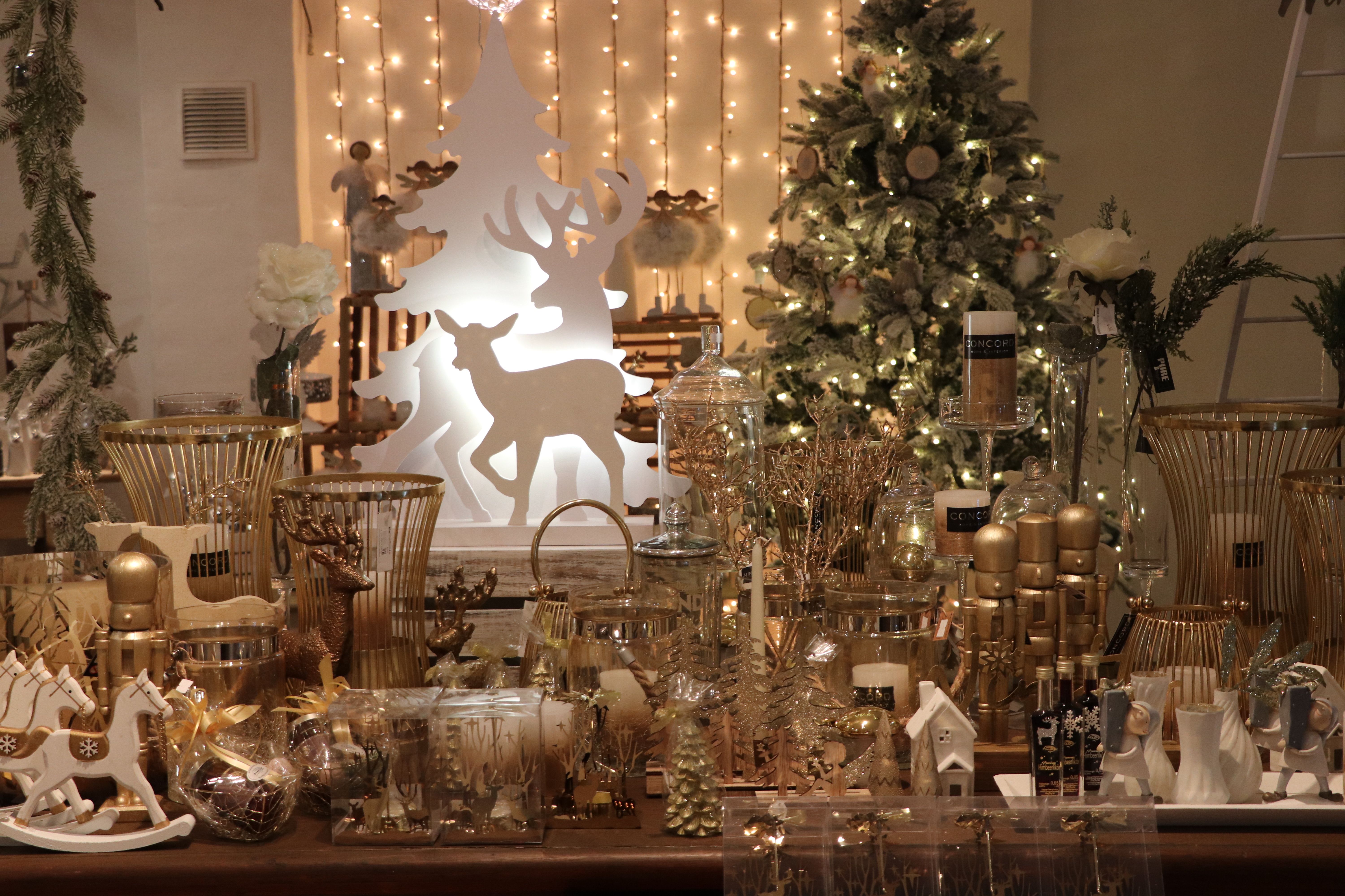 Vánoční dekorace se zlatými a bílými prvky, včetně svíček, sobů a vánočního stromku v pozadí.