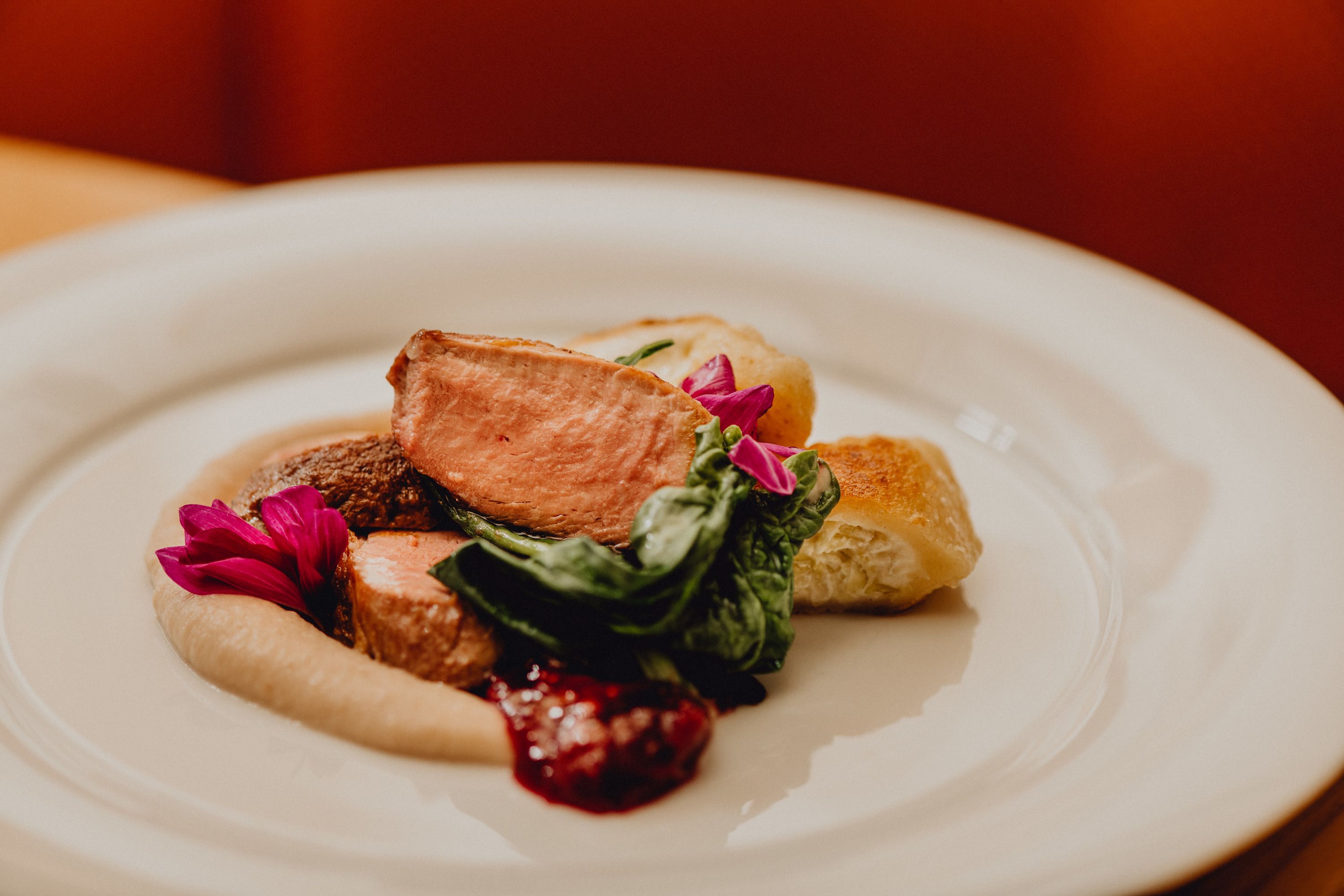 Talíř s růžovou pečenou kachnou, smetanovými tartaletkami, kaštanovým pyré a zelenými listy, zdobený jedlými květy.