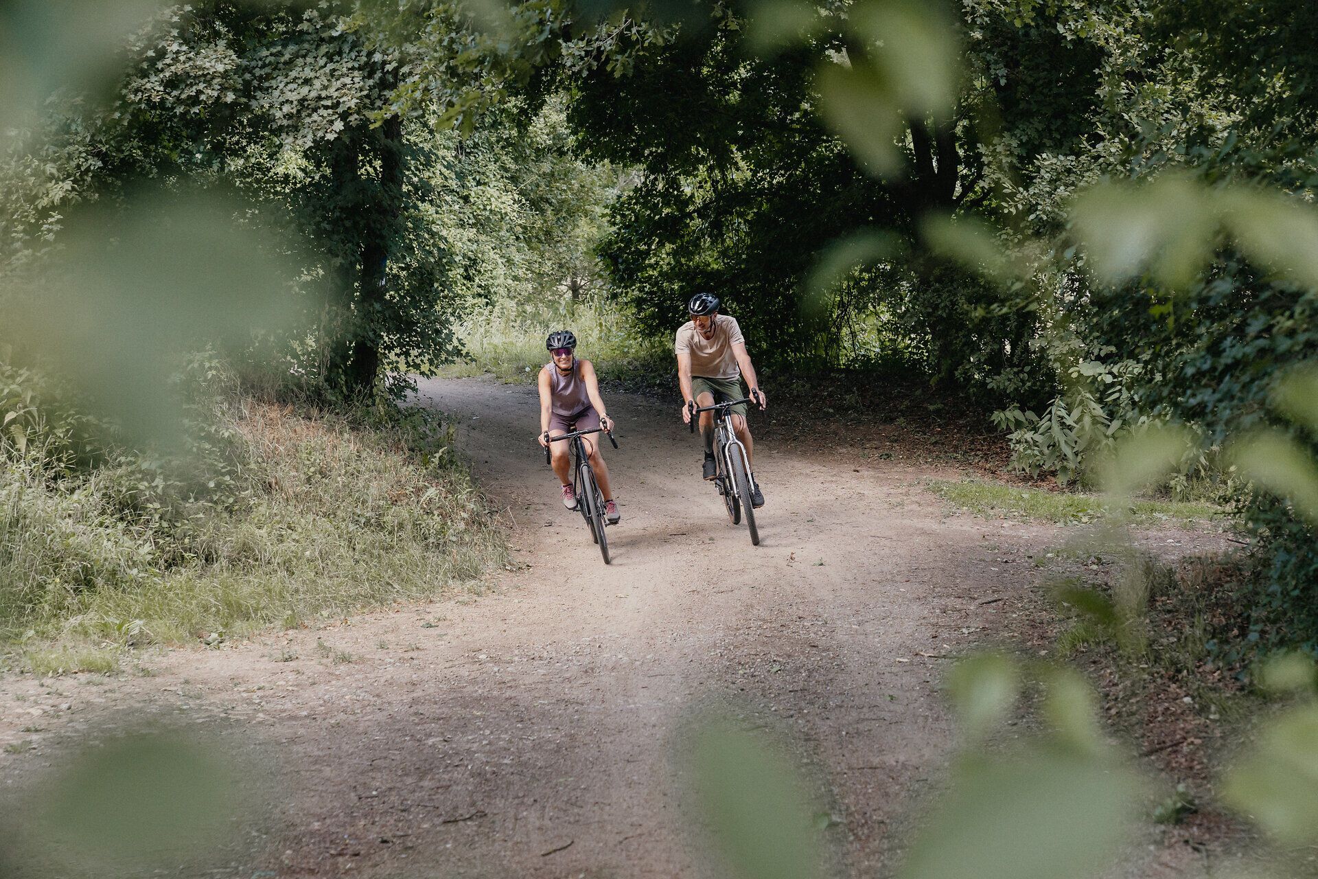 Dva cyklisté na lesní cestě v zeleném prostředí.