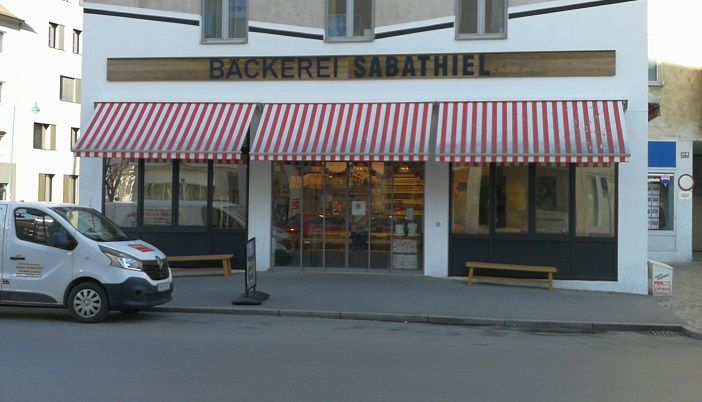 Pohled na pekárnu Sabathiel zvenčí s červenobíle pruhovanou markýzou a dodávkou před ní.