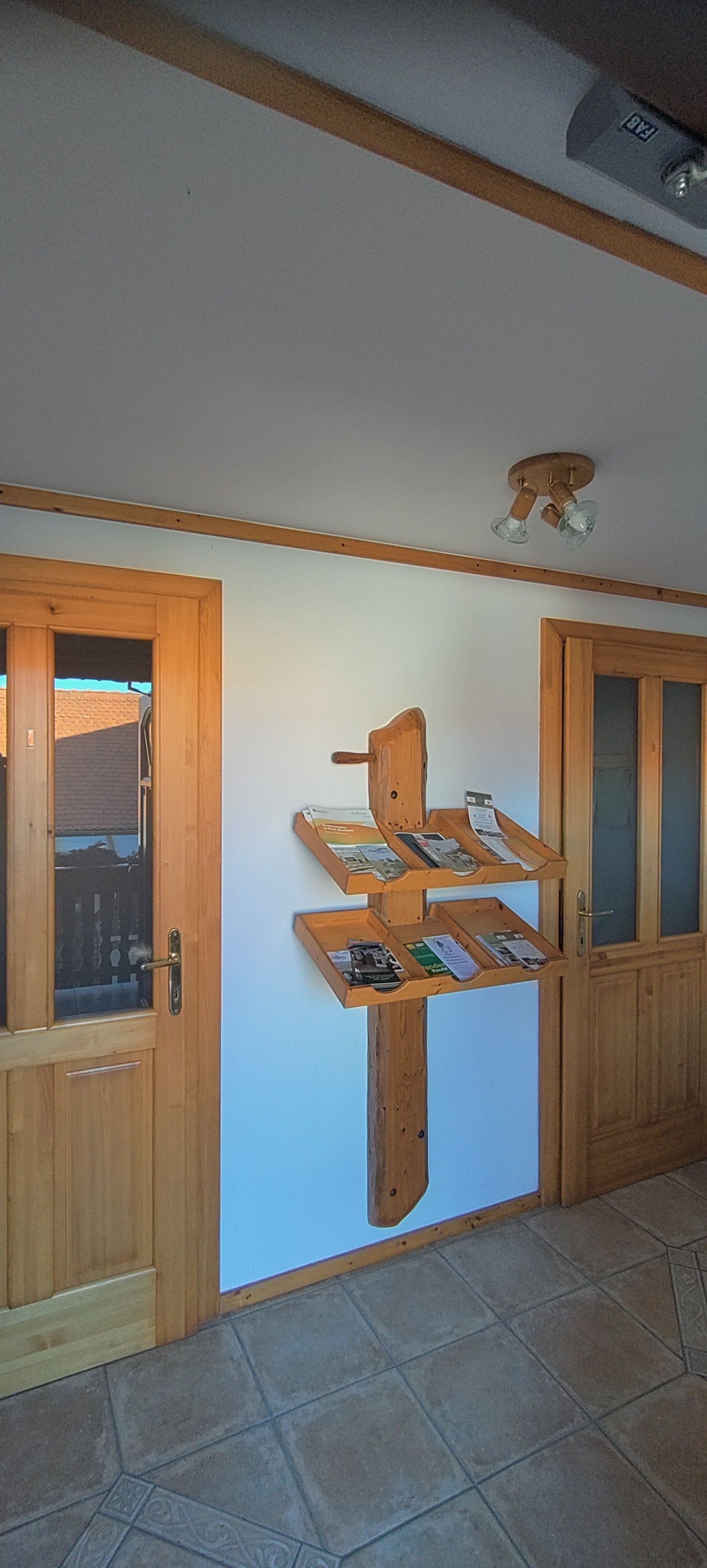 Dřevěná police s brožurami na bílé stěně mezi dvěma dřevěnými dveřmi.