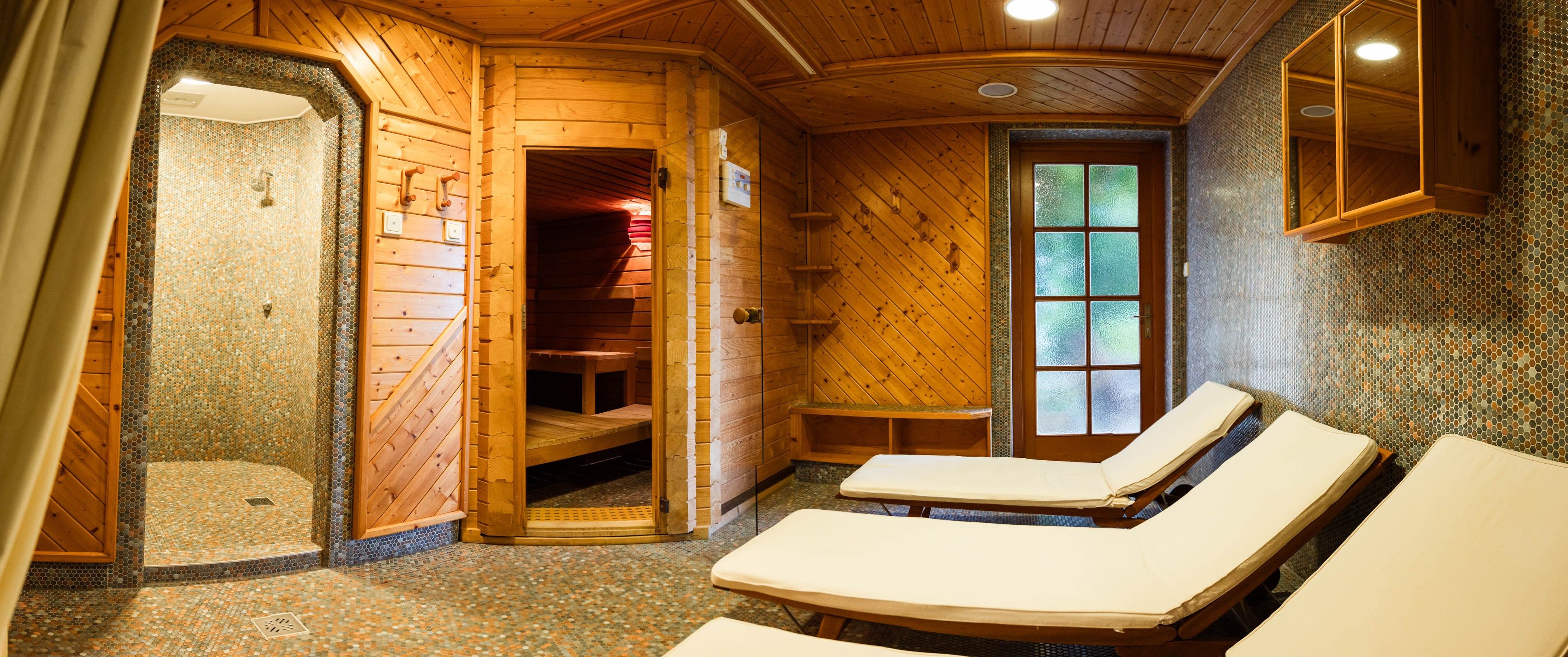 Útulná sauna s dřevěným obložením, lehátky a sprchou.