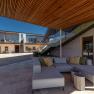 Vnitřní dvůr moderní budovy s dřevěnými prvky, skleněným zábradlím a šedým sedacím nábytkem.