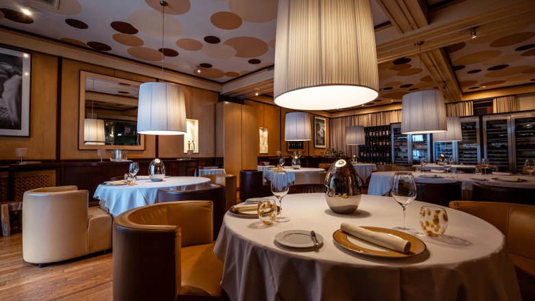 Elegantní restaurace s kulatými stoly, bílými ubrusy a velkými závěsnými lampami.