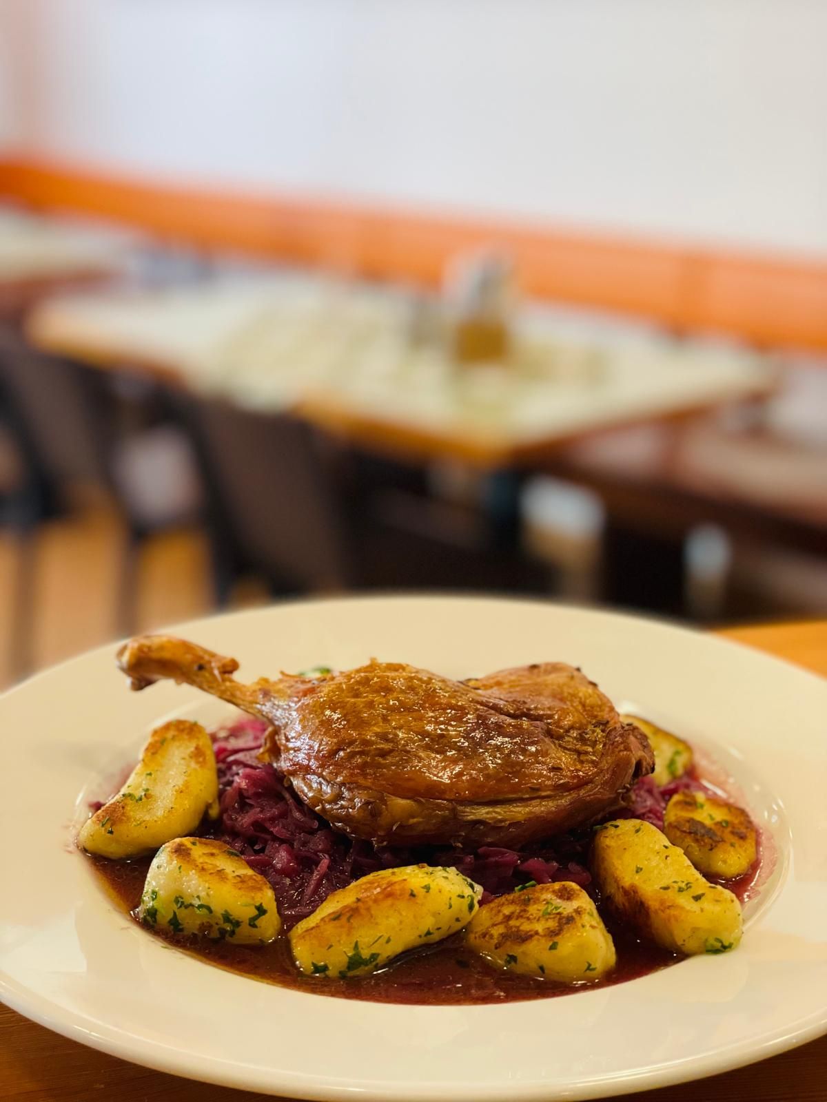 Talíř s pečeným kachním stehýnkem, bramborovými knedlíky a červeným zelím v restauraci.