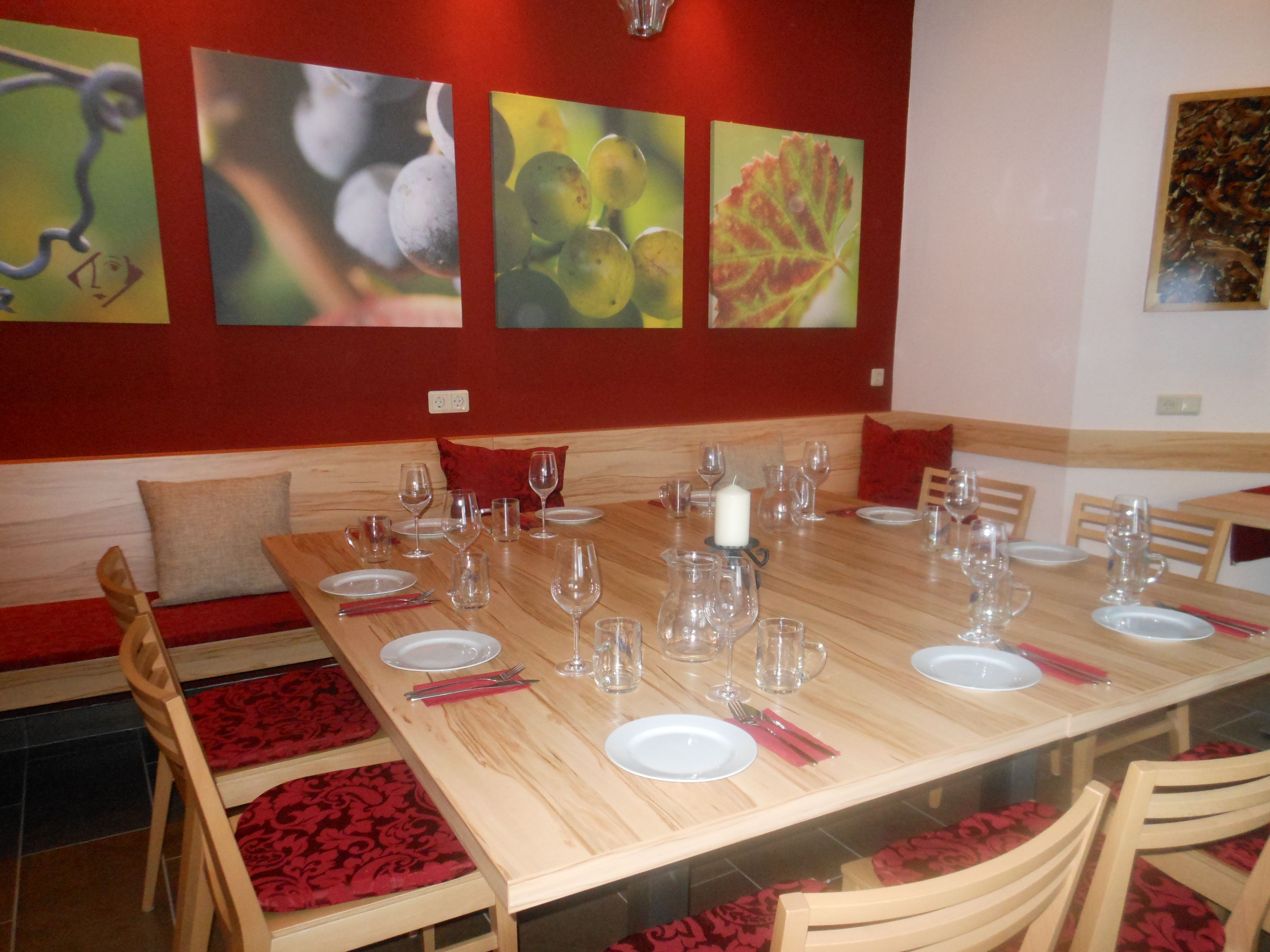 Degustační místnost se zastřešeným dřevěným stolem, sklenicemi na víno a nástěnnými malbami hroznů.