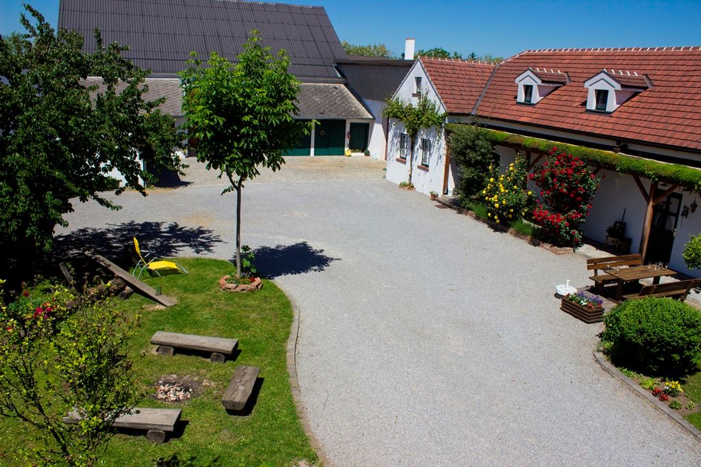 Udržované nádvoří se stromy, květinami a posezením, obklopené budovami s červenými střechami.