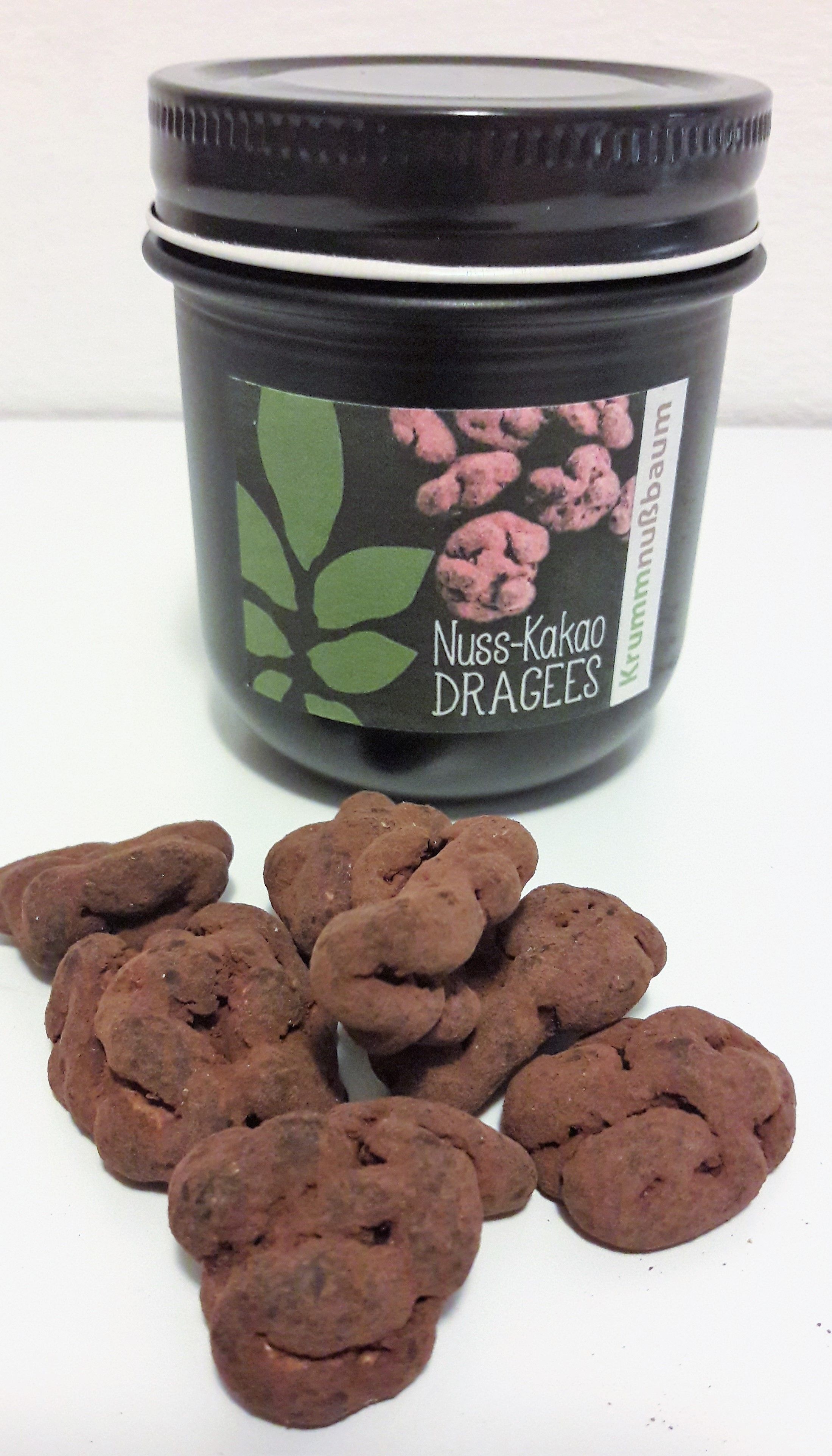 Sklenice s nápisem "Nuss-Kakao Dragees" a několik dražé před ní.