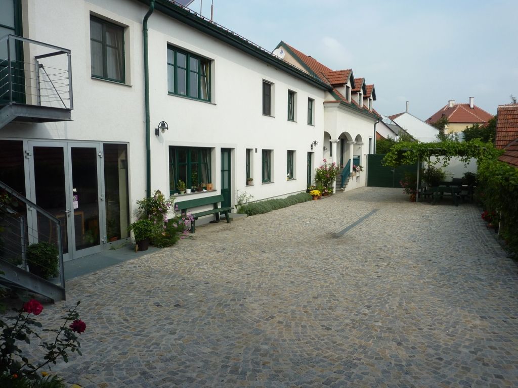 Vnitřní dvůr vinařství s dlážděnou podlahou, bílými budovami a zelenými okenními rámy.