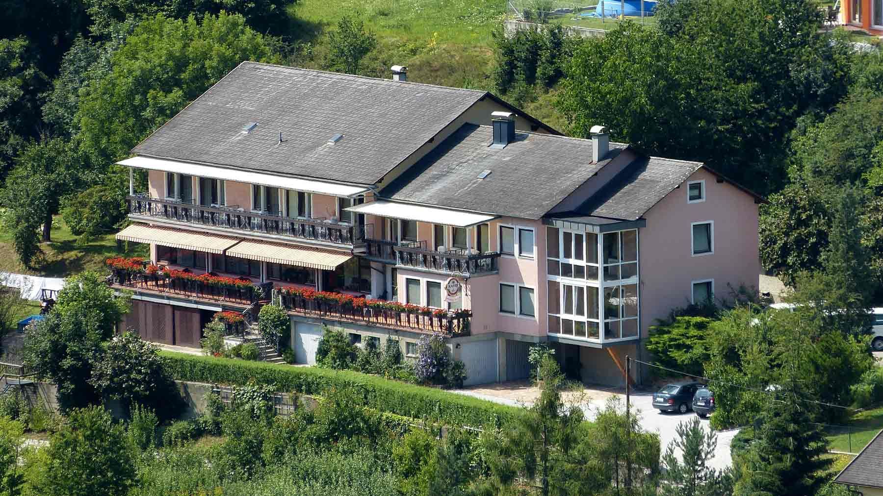 Velký dům s balkonem a zahradou, obklopený stromy.