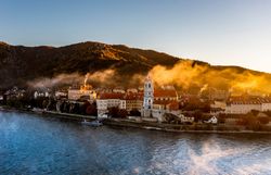 Die sanften Hügel umarmen das malerische Städtchen, während die Morgensonne die Nebelschwaden sanft vertreibt. Die historischen Gebäude, umgeben von üppigem Grün, laden zu einem unvergesslichen Spaziergang ein, der die Seele berührt.